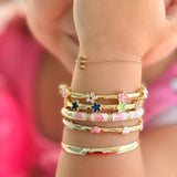 Child's arm wearing multiple gold bracelets with floral designs.
