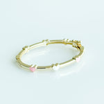 Gold bracelet with pink and white beads on a light gray background