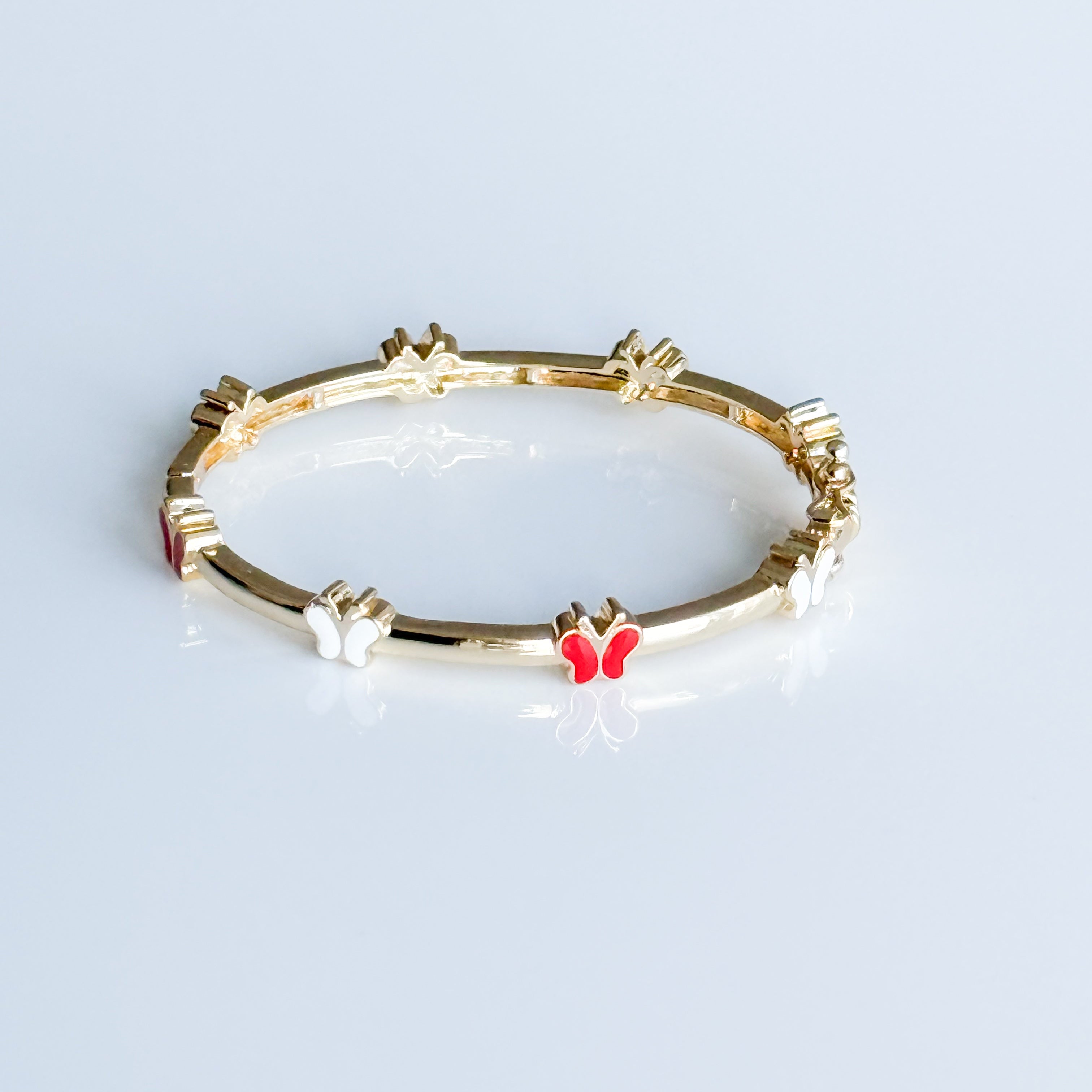 Gold bracelet with a red butterfly charm on a light gray background