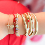 Gold bracelets with star and heart charms on a wrist against a red fabric background