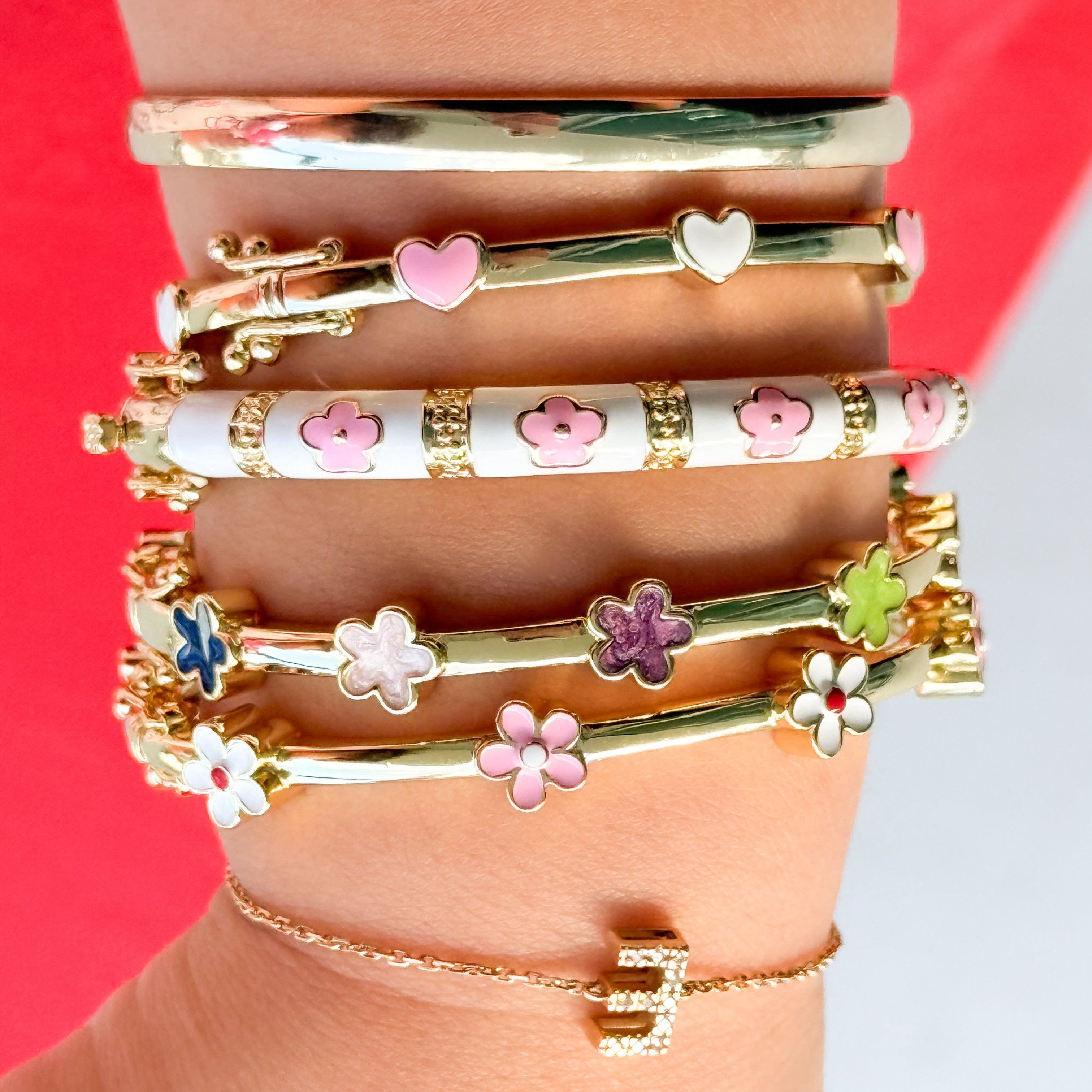 Stack of gold bracelets with floral and heart designs on a red and white background