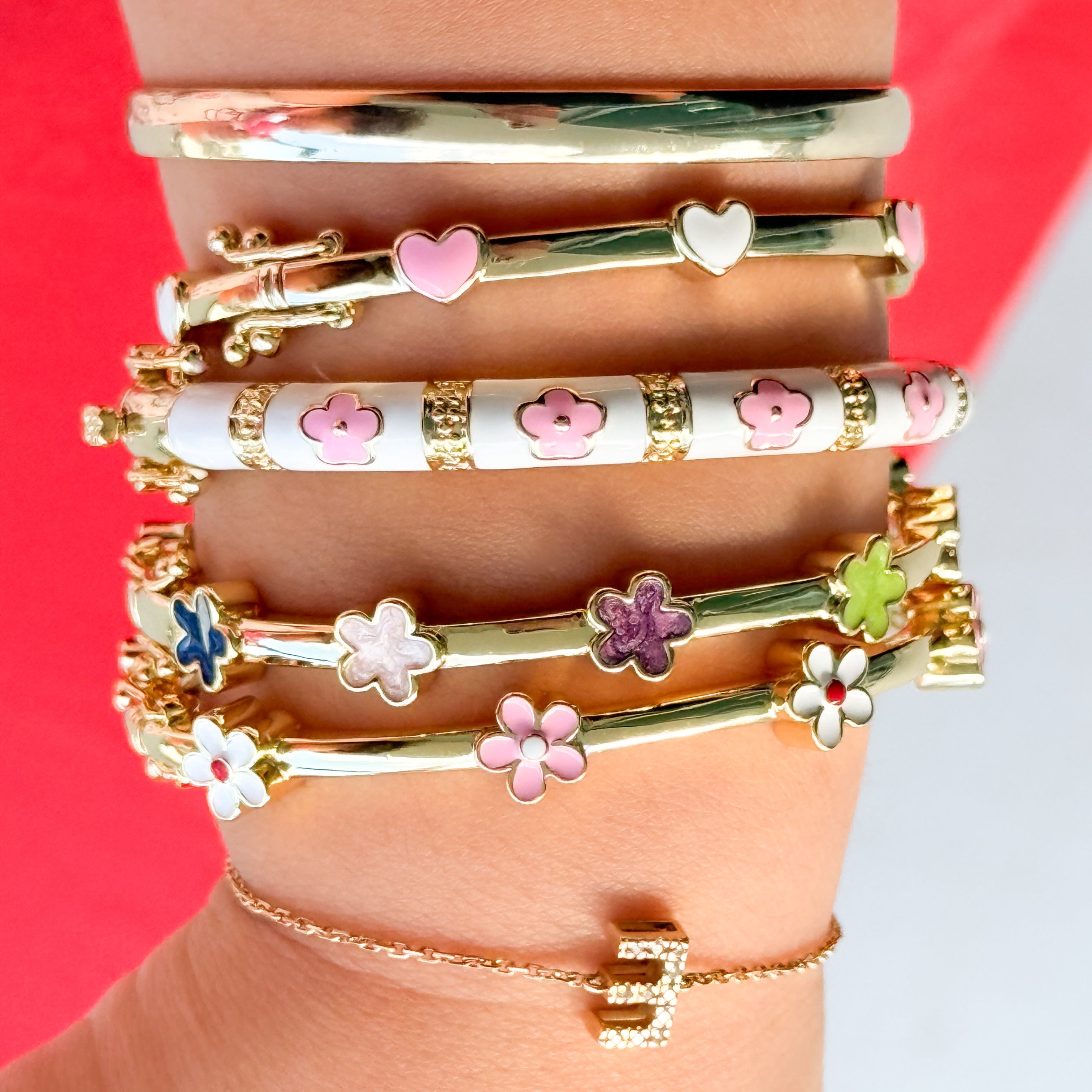 Stack of gold bracelets with floral and heart designs on a red and white background
