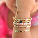 Child's arm wearing multiple gold bracelets with floral designs.