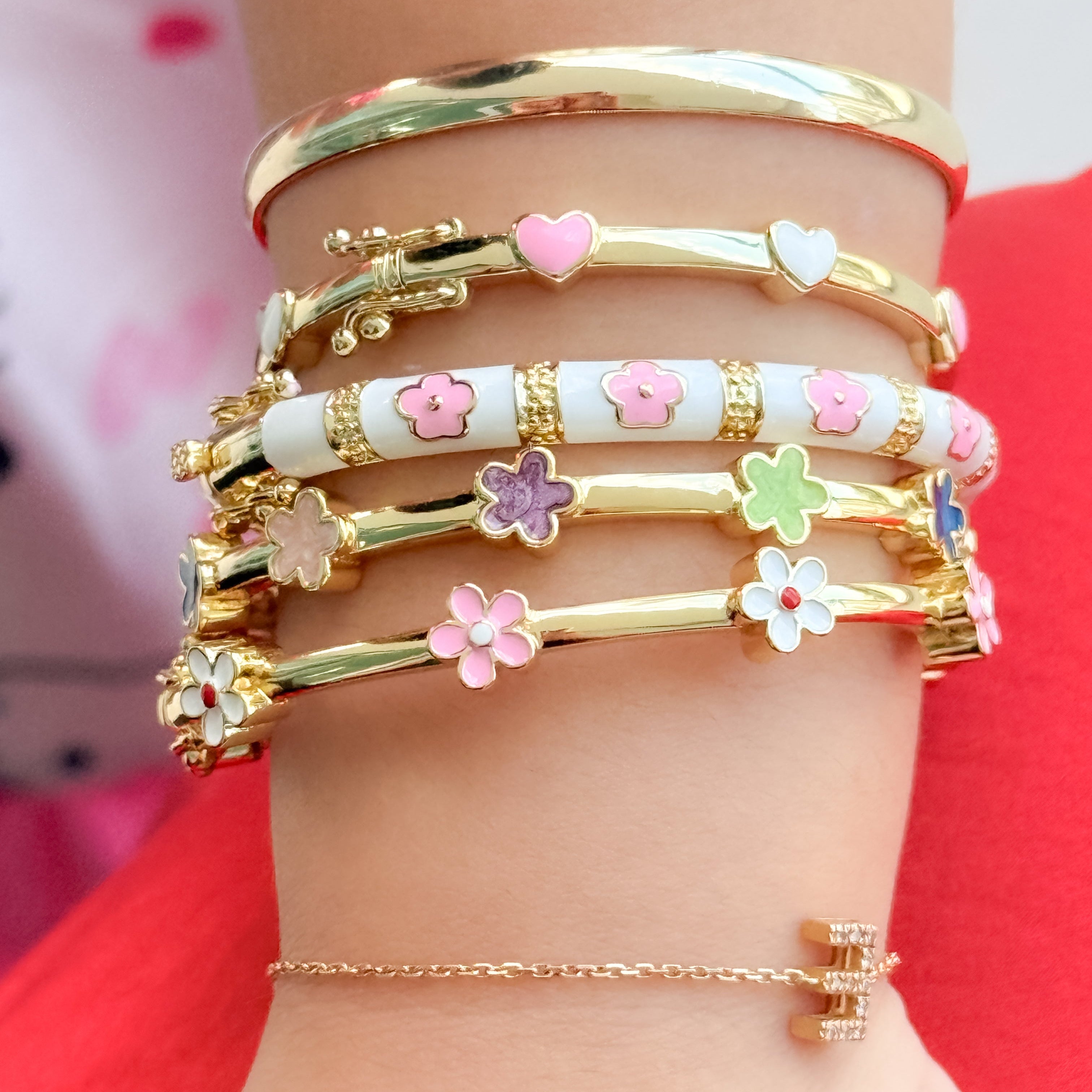 Gold and colorful floral bracelets on a wrist against a red background