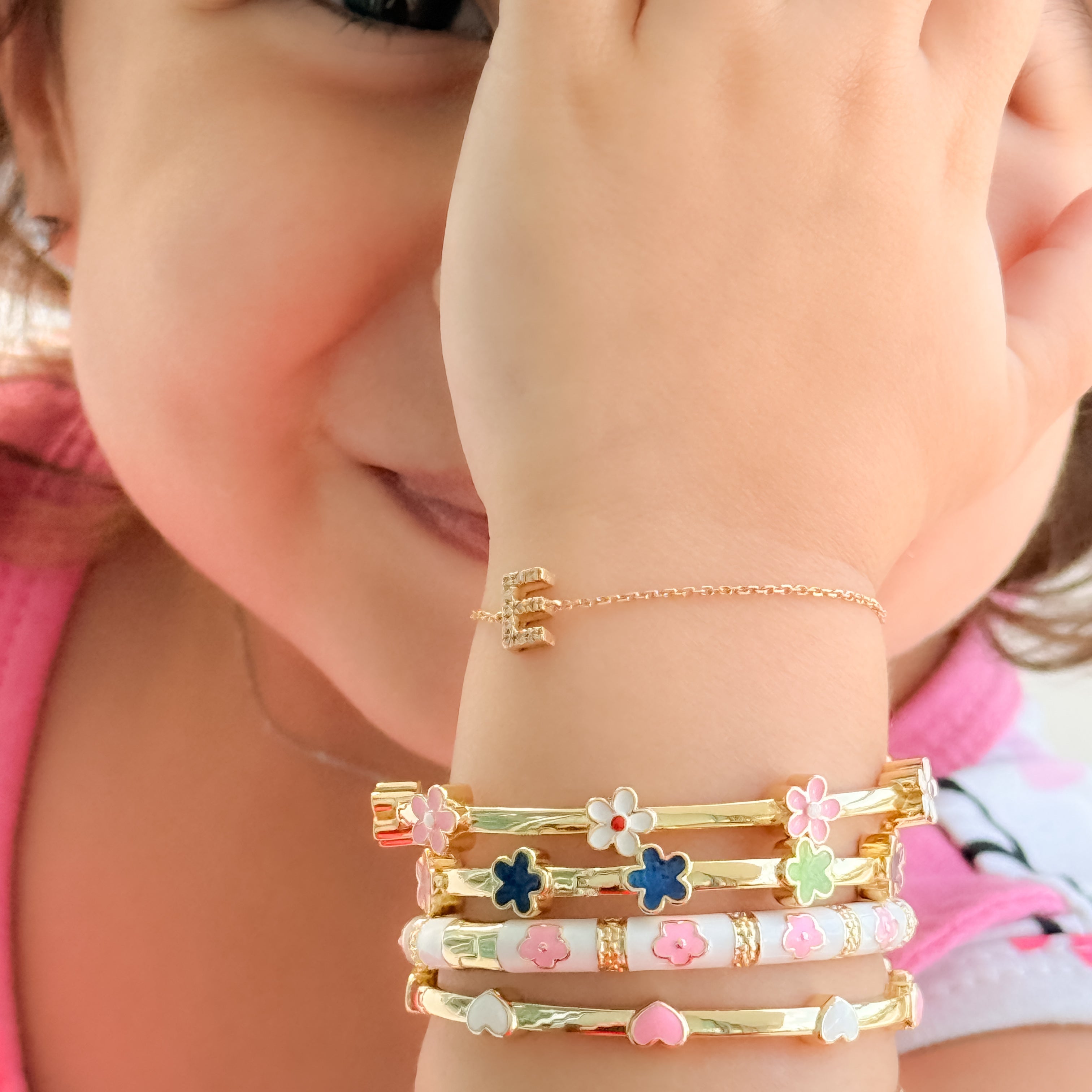 Child's arm wearing multiple gold bracelets with floral designs.