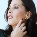 Woman wearing gold jewelry including earrings, ring, and bracelets against a light blue background