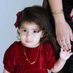 Child in a red dress holding hands with an adult against a neutral background