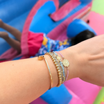 pink crystal saint benedict bracelet layered with gold bracelets on wrist




