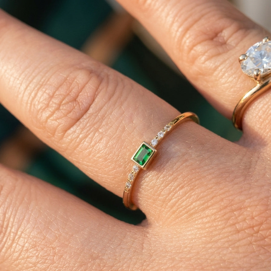 Elegant green emerald cut CZ ring in 14K yellow gold worn on hand outdoors