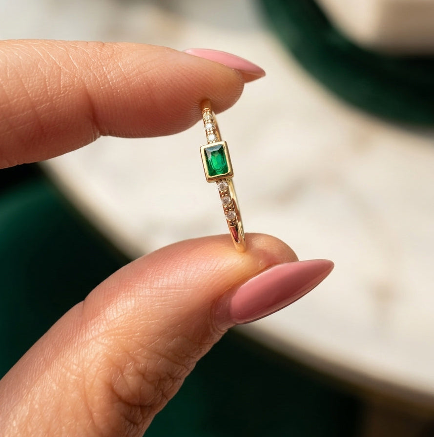 14K gold emerald-colored ring with zirconia accents held between fingers in natural light, featuring a delicate minimalist fine jewelry design.