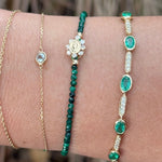 Close-up of a wrist wearing three green gemstone bracelets with a blurred natural background