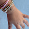 Hand wearing multiple bracelets on a light blue background