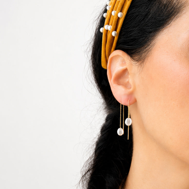 Woman wearing 14K solid yellow gold genuine pearl threader earrings featuring 7.4 mm freshwater pearls and a 2.75-inch pull-through chain design, styled for an elegant everyday fine jewelry look.