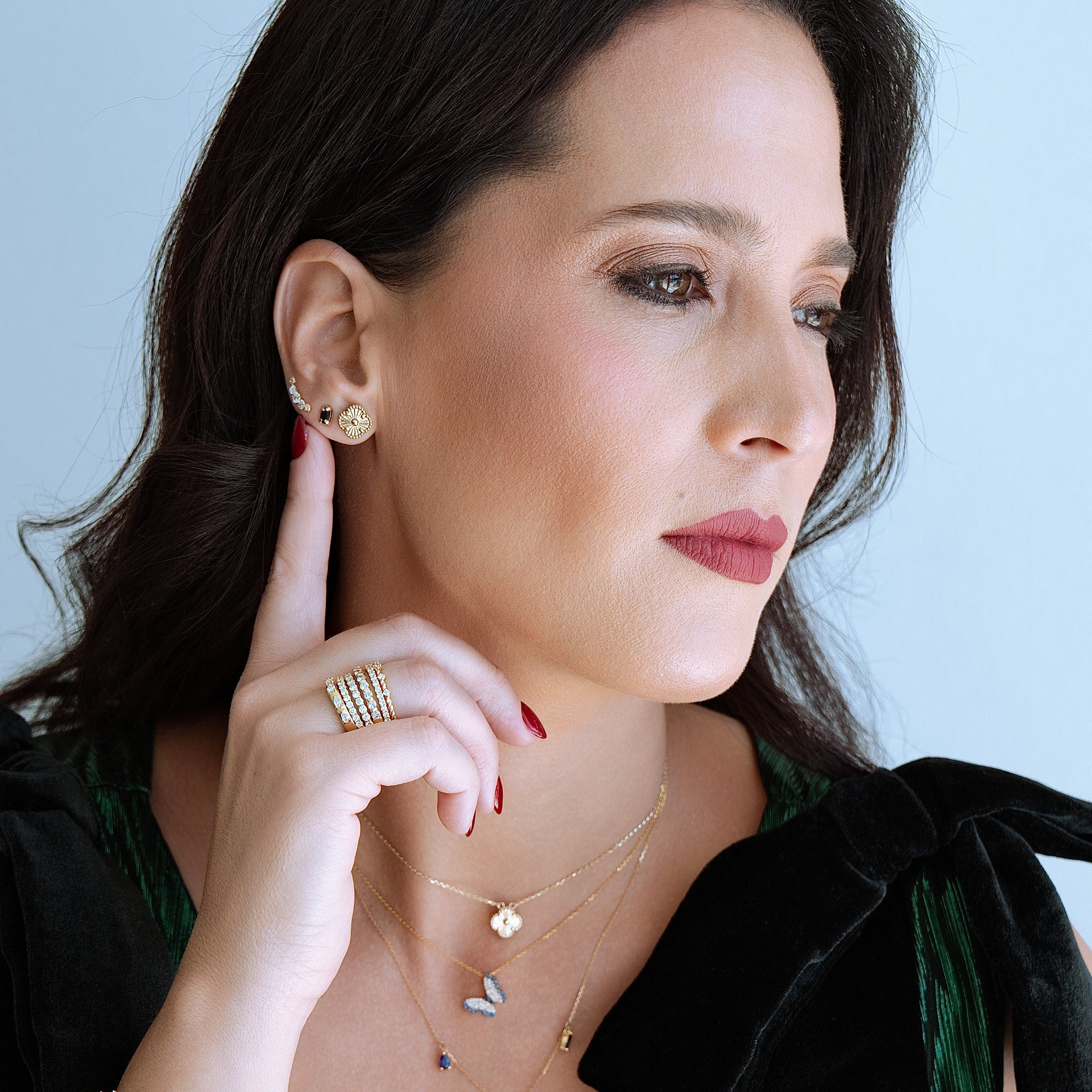 Woman wearing gold jewelry including earrings, ring, and bracelets against a light blue background