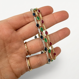 Hand wearing gold bracelets with colorful gemstones on a white background