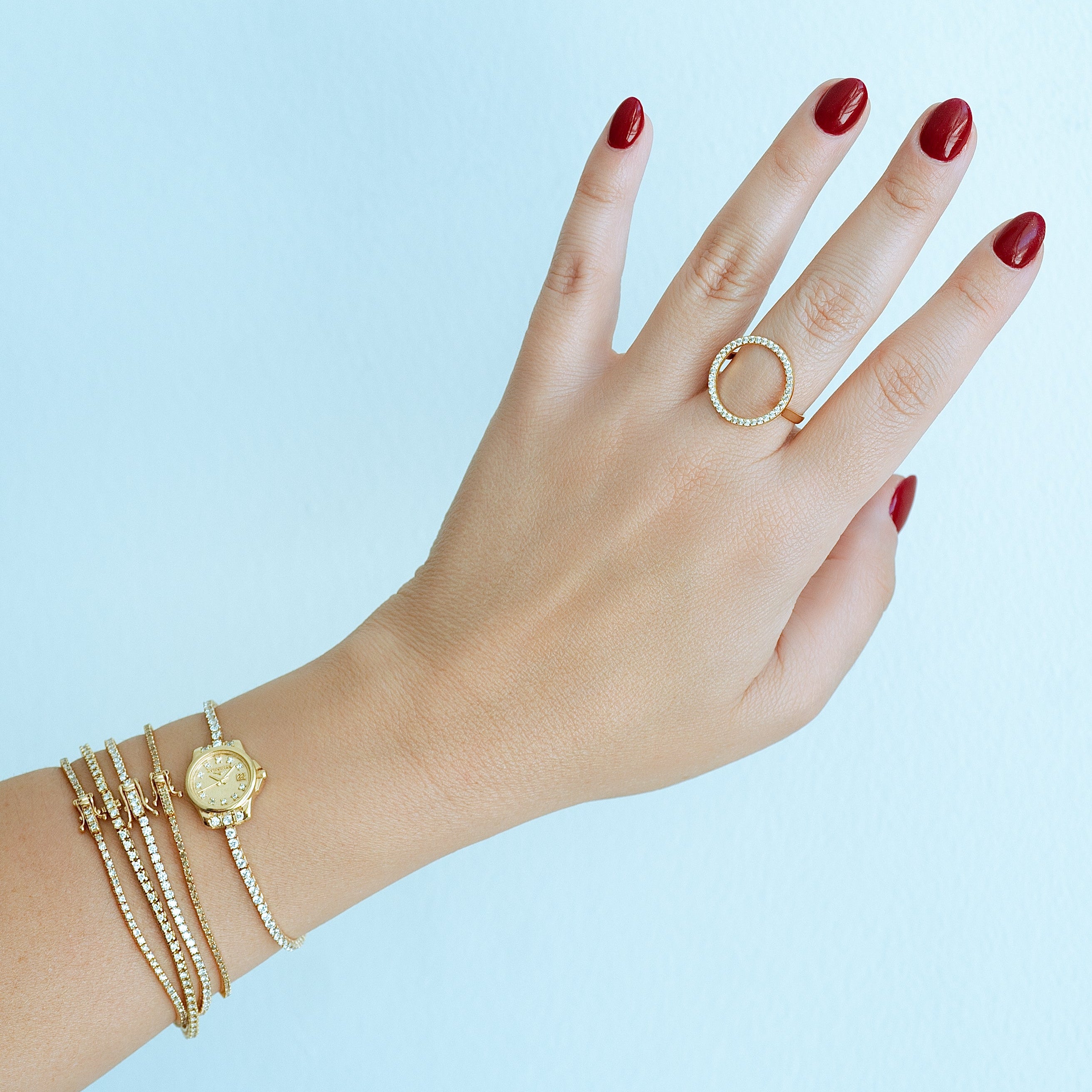Hand wearing gold rings and bracelets against a light blue background