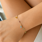 Woman wearing an 18K solid yellow gold multi-gemstone bracelet featuring natural garnet, blue topaz, citrine, peridot and amethyst dangling gemstone charms