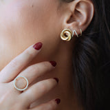 Close-up of a woman wearing gold spiral earrings with her hand near her face.