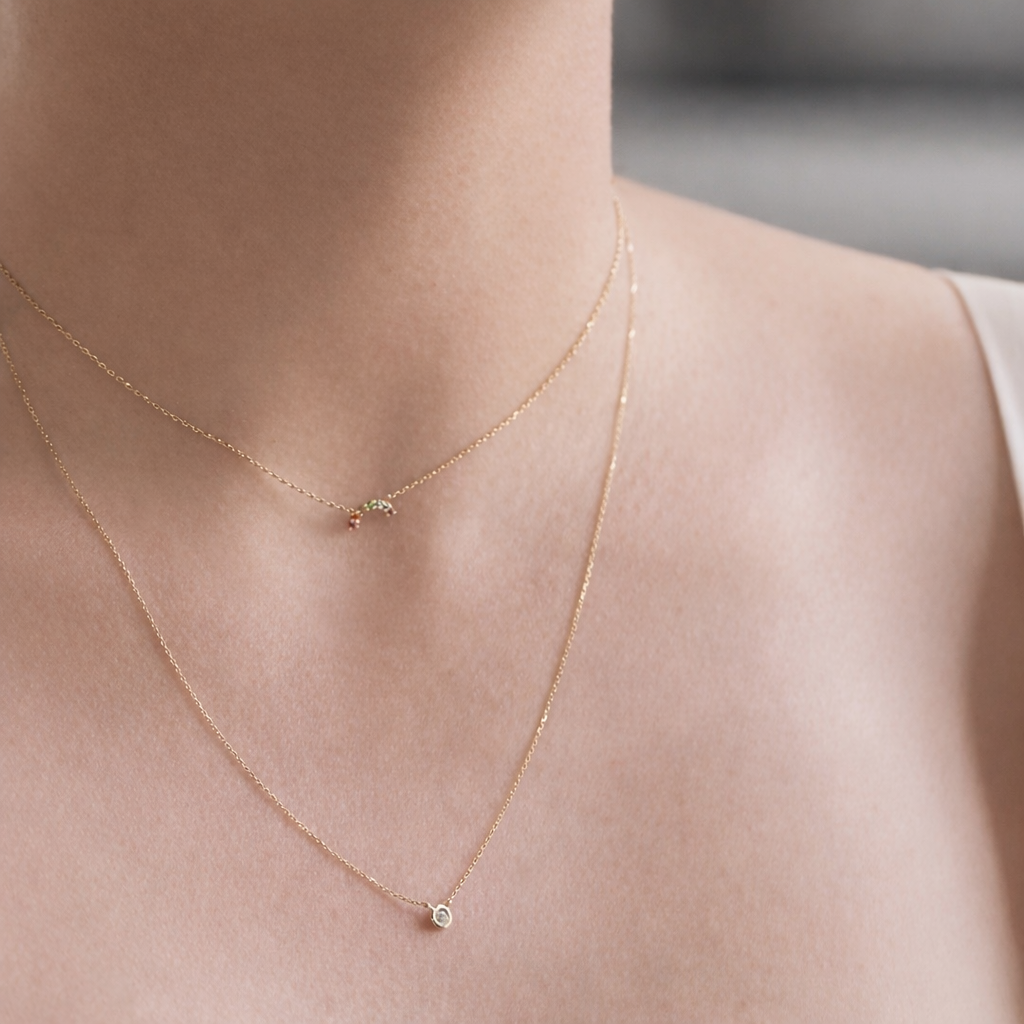 Gold necklace with small pendants on a person's neck against a neutral background