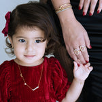 Child in a red dress with a woman's hand holding a ring, against a neutral background