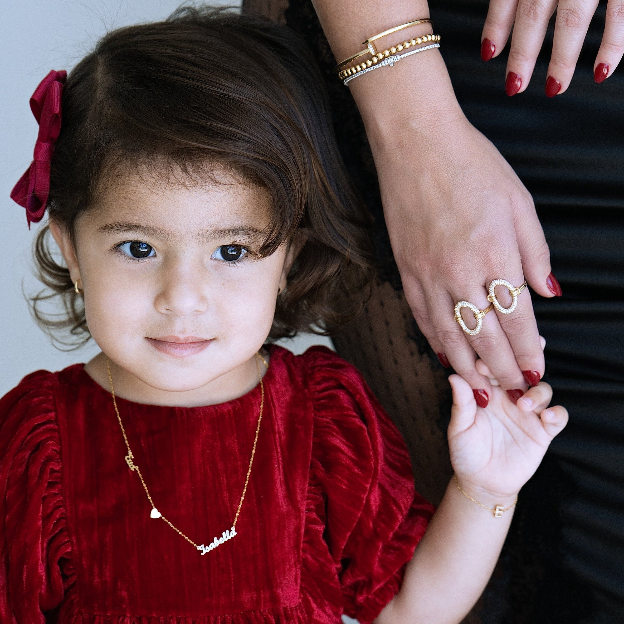 Child in a red dress with a woman's hand holding a ring, against a neutral background