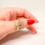 Hand wearing multiple gold rings with red nail polish on a light background