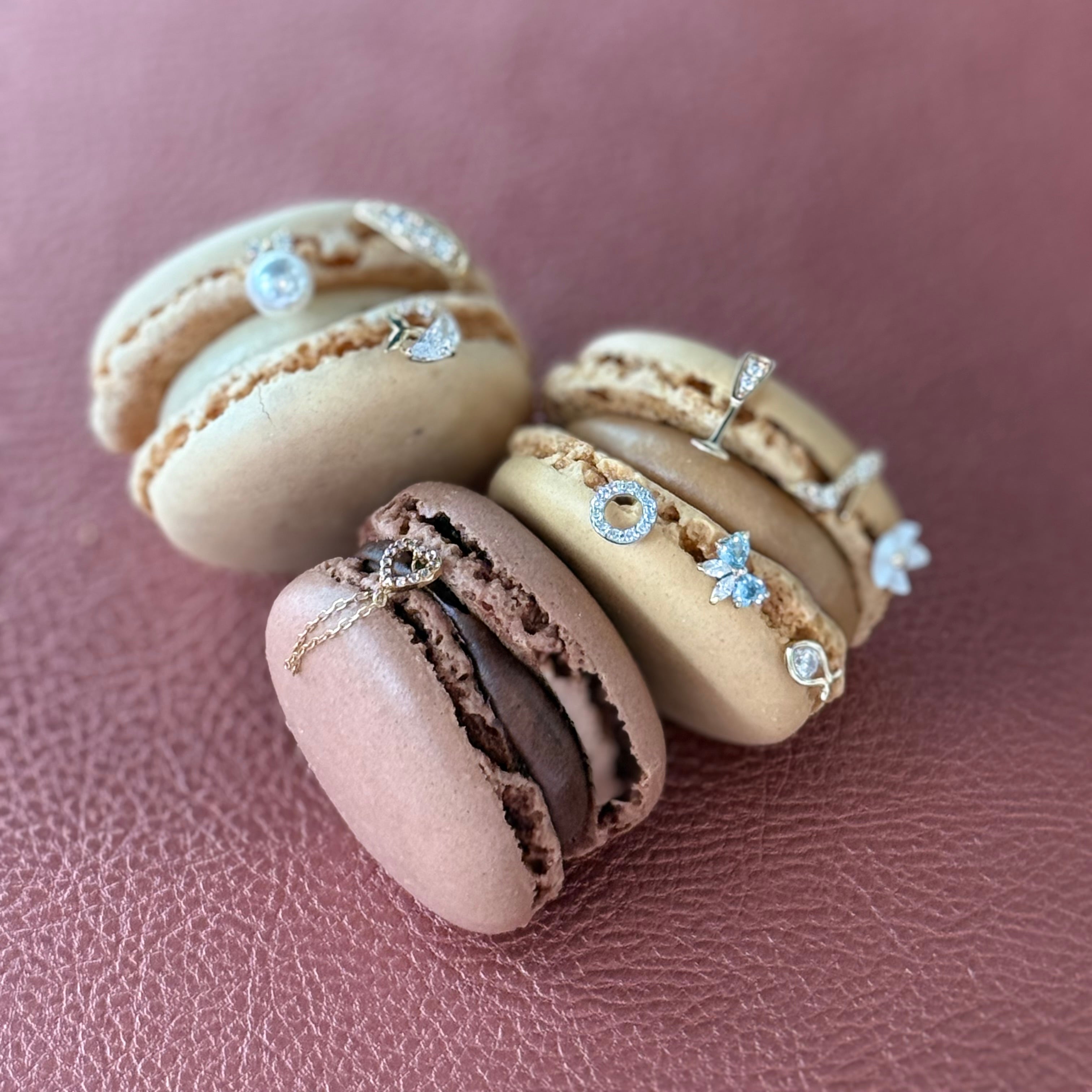 Macaron-shaped earrings with gemstone details on a pink surface