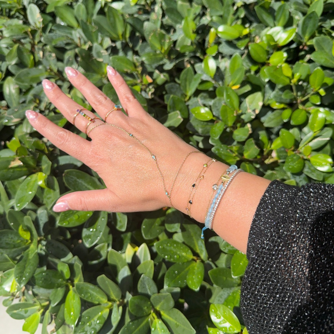 Blue topaz macramé bracelet with gold miraculous medal charm worn on wrist layered with delicate gold bracelets.

