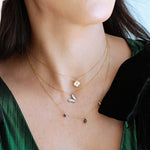 Close-up of a woman wearing multiple gold necklaces with small pendants against a green garment.