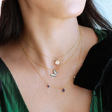 Close-up of a woman wearing multiple gold necklaces with small pendants against a green garment.