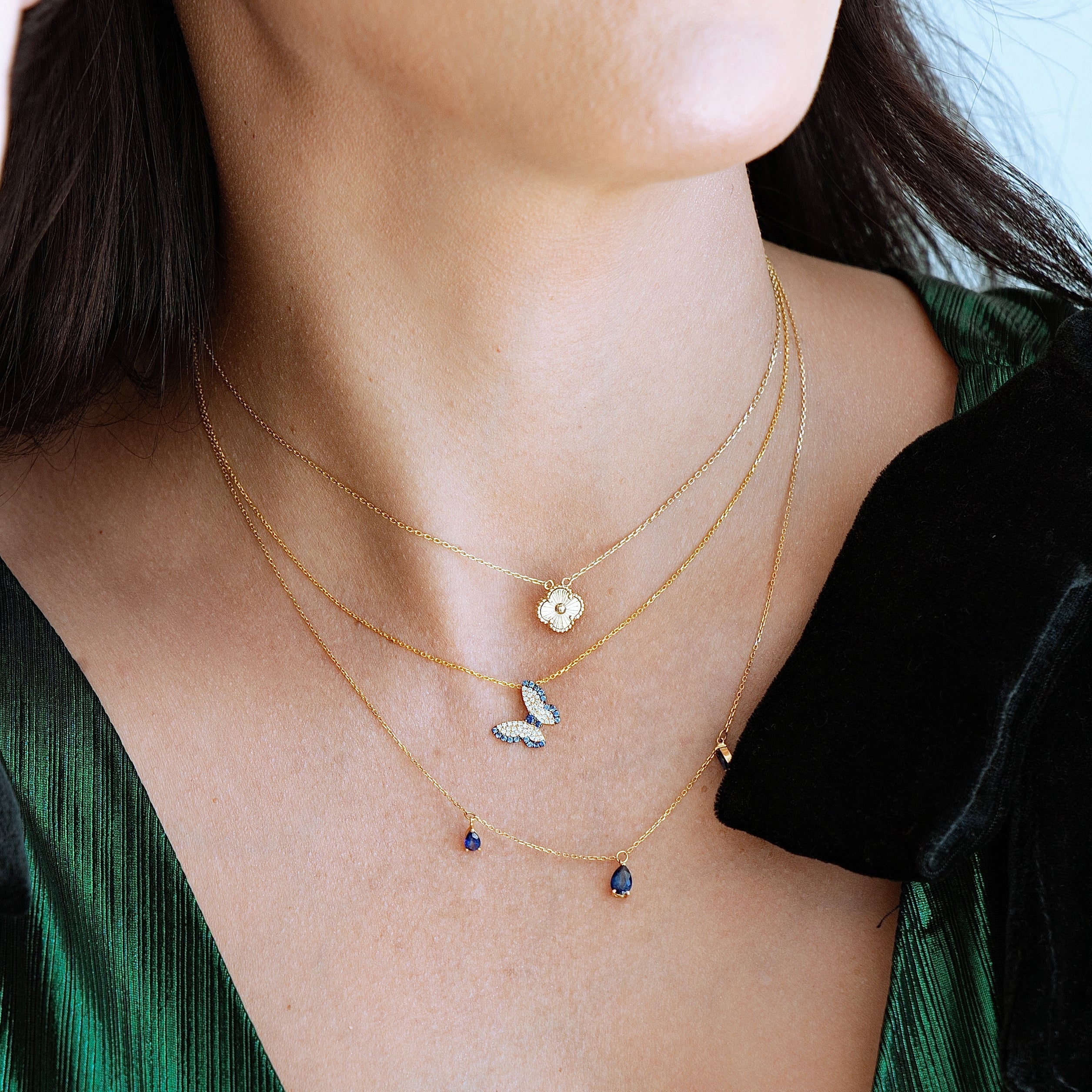 Close-up of a woman wearing multiple gold necklaces with small pendants against a green garment.