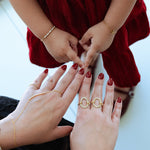 Two pairs of hands with rings and red nail polish on a light background