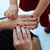 Close-up of hands with gold rings and red nail polish, wearing gold bracelets.