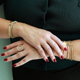 Close-up of a person's hands wearing gold bracelets and rings on a plain background