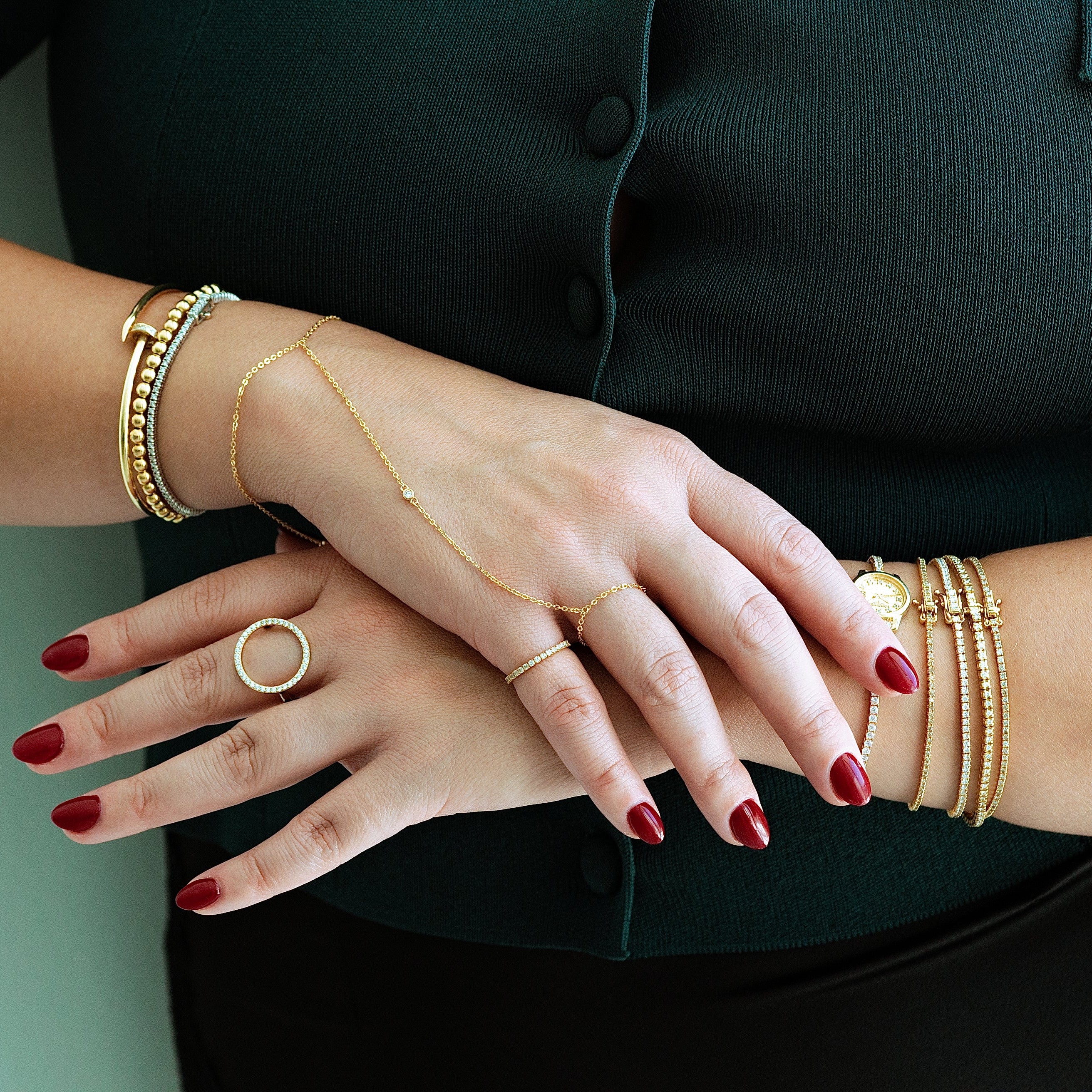 Close-up of a person's hands wearing gold bracelets and rings on a plain background