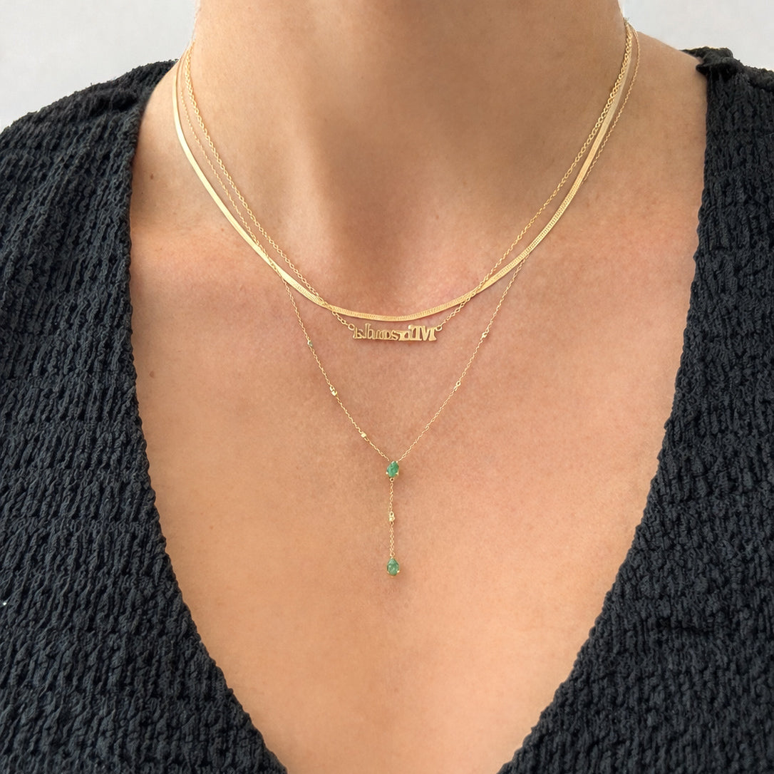 3mm micro block gold plated name necklace layered with delicate gold chains and emerald drop necklace on skin