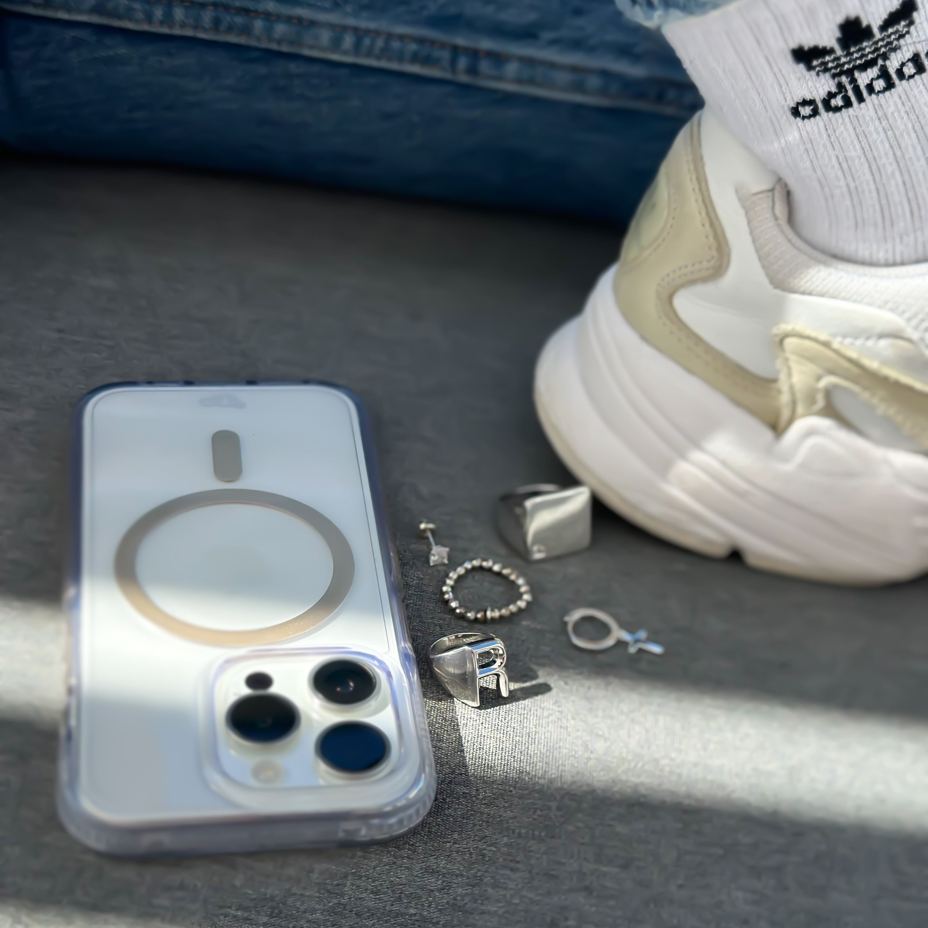A 925 sterling silver ring with elastic balls and princess cut cubic zirconia, displayed next to a smartphone and a shoe on a surface with light reflections.