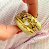 Macaron with gold decorations held by a hand on a pink striped background