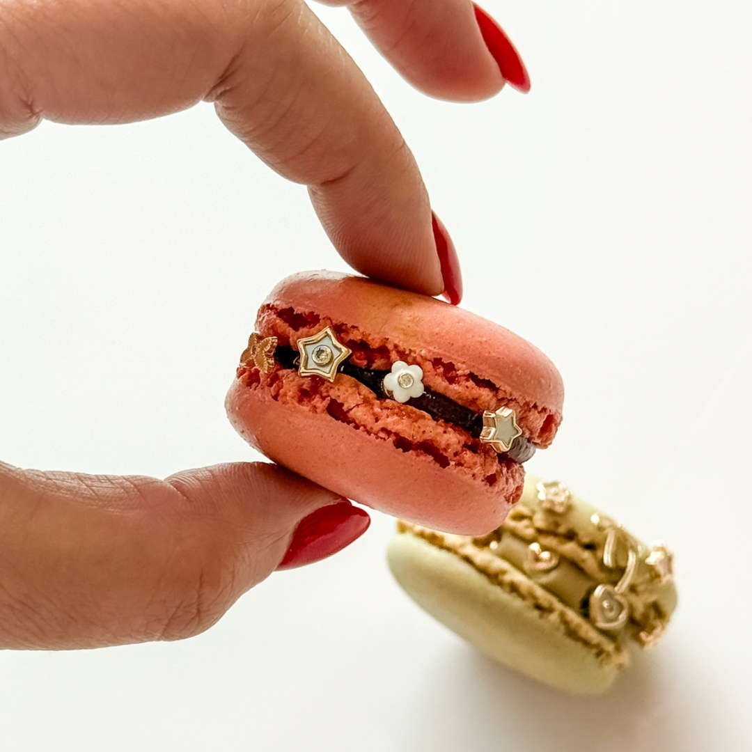 Hand holding a pink macaron with gold decorations on a white background