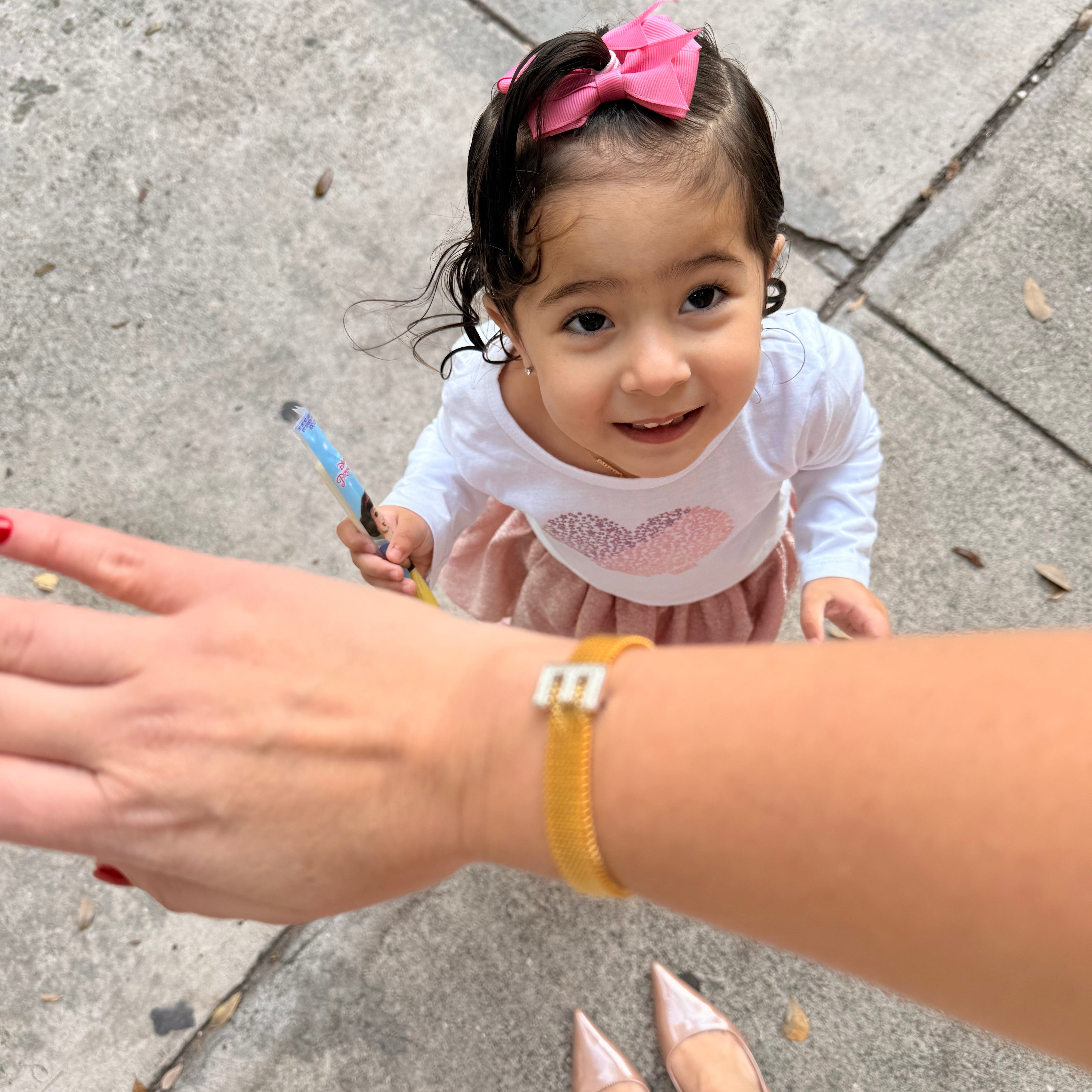 Child holding a toy with an adult's hand on a sidewalk