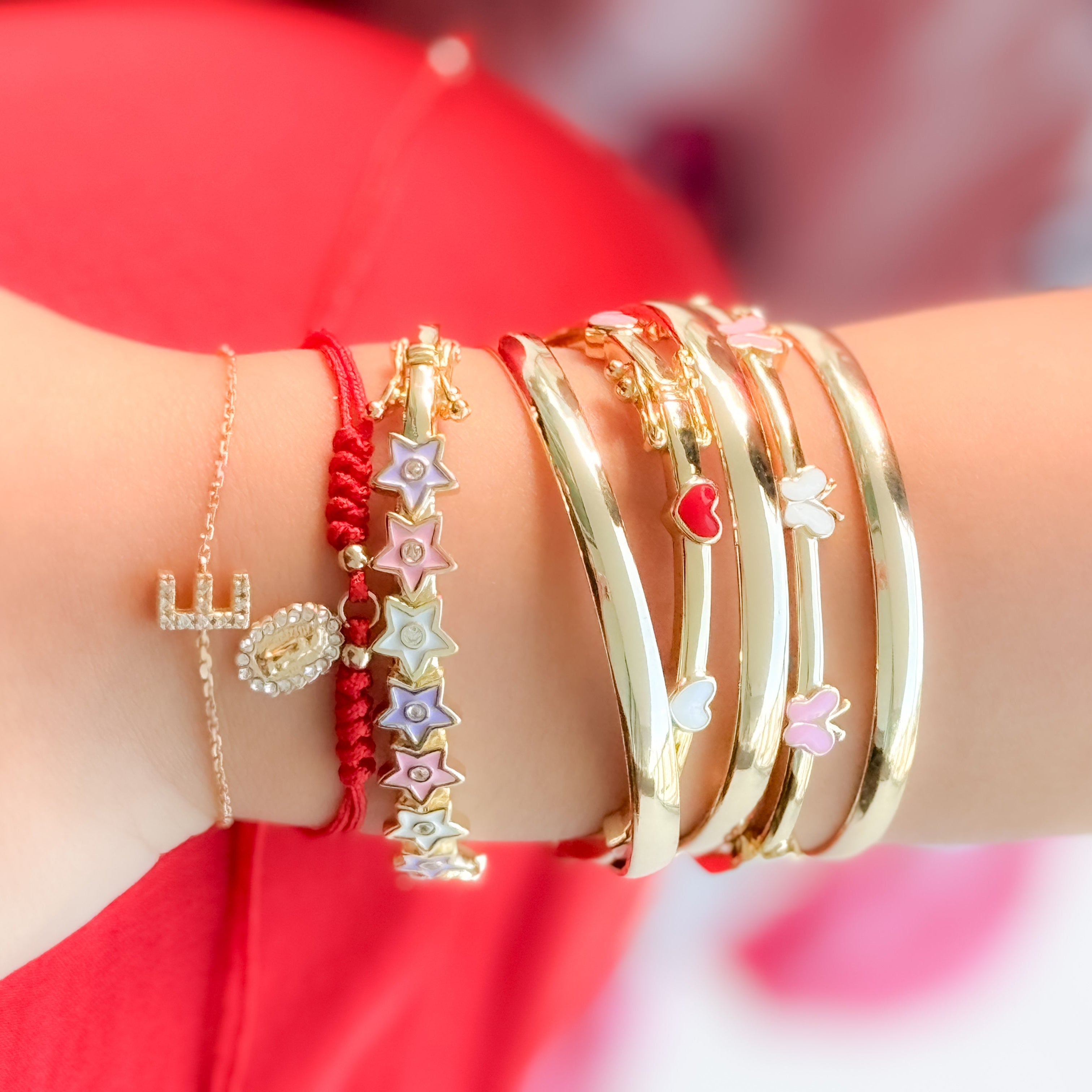 Gold bracelets with star and heart charms on a wrist against a red fabric background