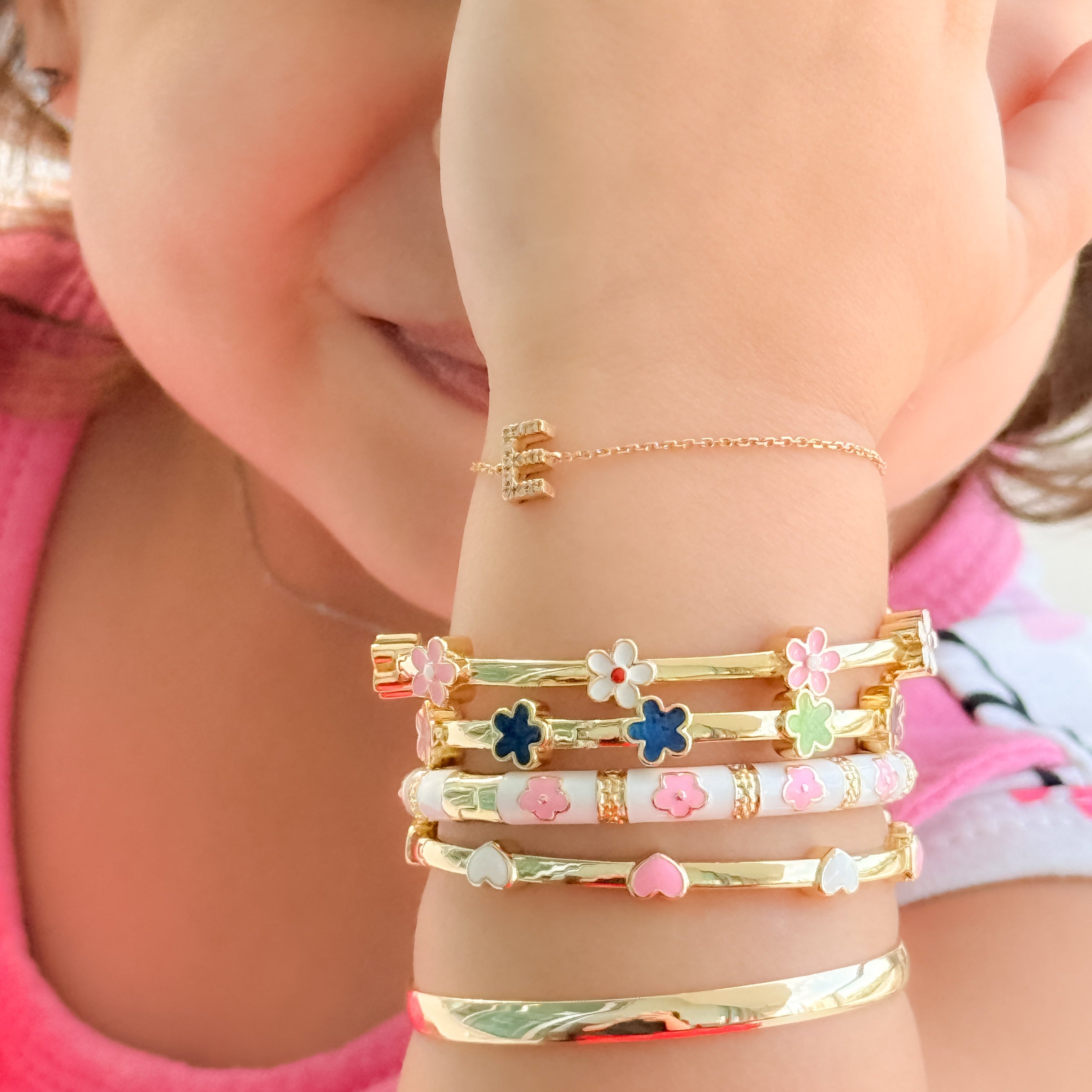 Child's arm wearing multiple gold bracelets with floral designs.