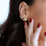 Close-up of a person wearing gold earrings and rings with a blurred background