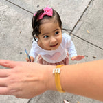 Child with a pink bow and white outfit on a sidewalk, with a hand reaching out.