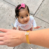 Child with a pink bow and white outfit on a sidewalk, with a hand reaching out.