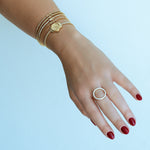 Hand wearing gold bracelets and a ring on a light blue background