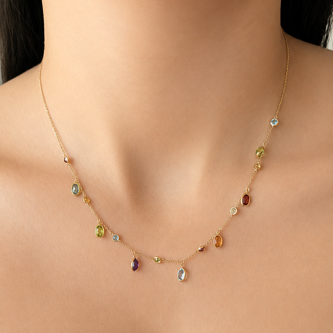 Woman wearing an 18K solid yellow gold multi-gemstone necklace featuring natural garnet, blue topaz, citrine, peridot and amethyst bezel-set charms