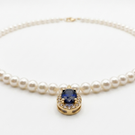 Close-up of an 18K solid yellow gold oval blue sapphire pendant accented by a halo of natural diamonds on a cultured pearl necklace.