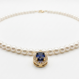Close-up of an 18K solid yellow gold oval blue sapphire pendant accented by a halo of natural diamonds on a cultured pearl necklace.