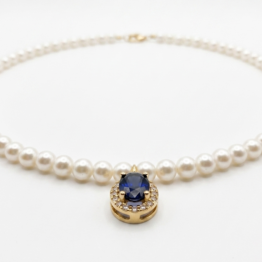Close-up of an 18K solid yellow gold oval blue sapphire pendant accented by a halo of natural diamonds on a cultured pearl necklace.